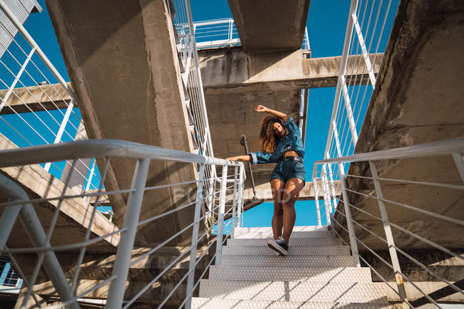 Joven mujer afroamericana en ropa de mezclilla bajando por una escalera de metal en la calle a la luz del día - foto de stock