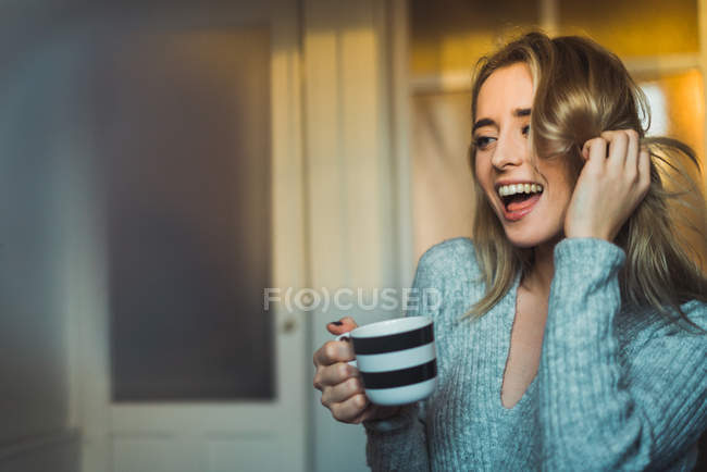 Joyeux jeune femme en pull tenant tasse de boisson — Photo de stock