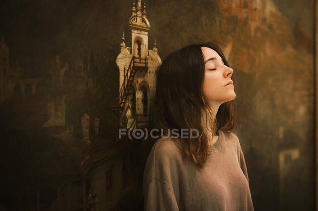 Vista laterale di bella giovane femmina guardando lontano mentre in piedi su sfondo sfocato di bella pittura in galleria d'arte — Foto stock