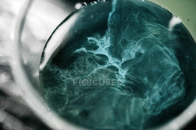 Closeup shot of glass of blue liquid after tattoo machine clean — Stock Photo