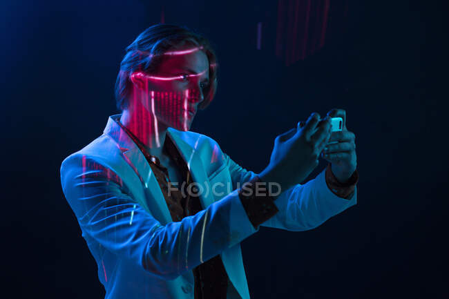 Abstract projection of face of attractive androgynous man in suit taking selfie in dark room — Stock Photo