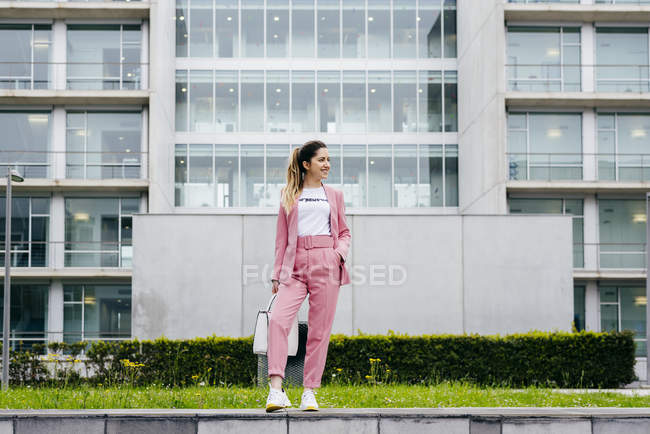 Elegante giovane donna in rosa in piedi di fronte a un moderno edificio per uffici — Foto stock