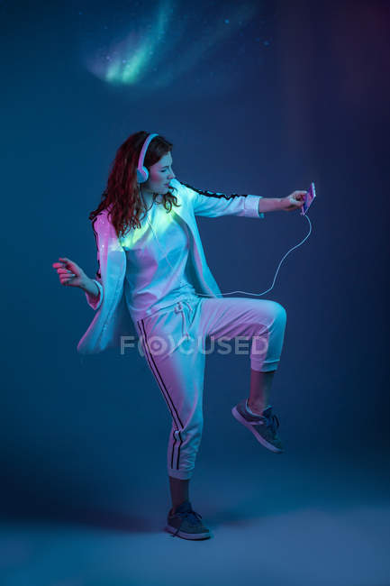 Женщина танцует со смартфоном и наушниками в неоновом свете — стоковое фото