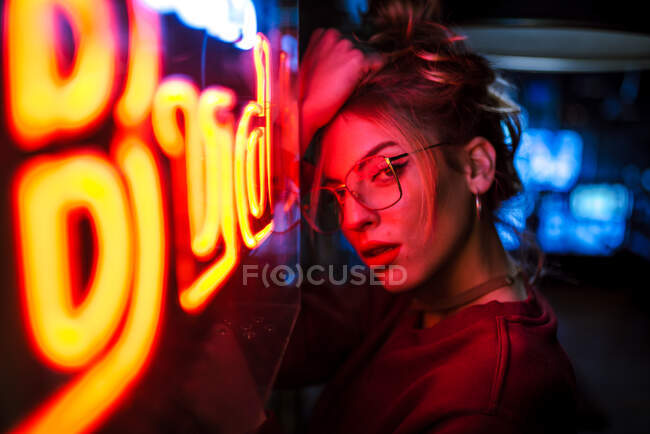 Vista laterale di donna attraente in occhiali con gli occhi chiusi appoggiati sulla parete al neon di illuminazione segno — Foto stock
