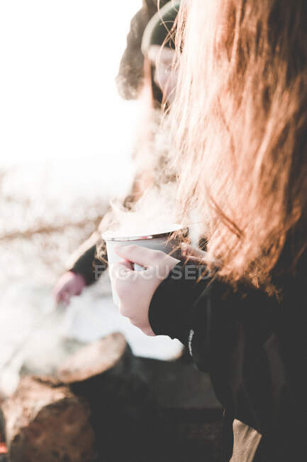 Crop vista laterale della donna con i capelli lunghi tenendo tazza fumante metallo alla luce del sole all'aperto — Foto stock