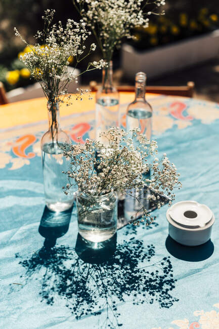 Piccoli fiori bianchi rustici in bottiglie di vino sul tavolo. — Foto stock