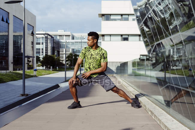 Afro-Américain échauffer les jambes dans la ville avec des bâtiments modernes sur fond — Photo de stock