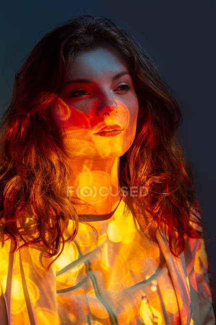 Pensive daydreaming woman standing in warm light and looking away in studio — Stock Photo