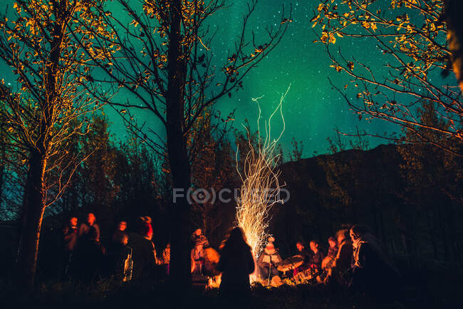 Group of people performing authentic ritual around burning and sparkling fire in dark woods with starry sky — Stock Photo