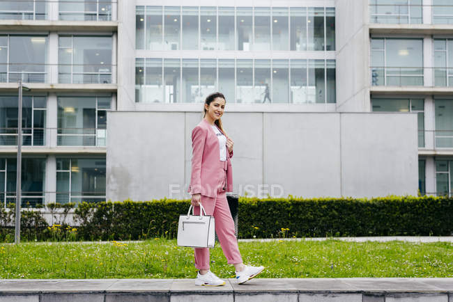 Femme élégante en costume rose debout devant un immeuble de bureaux moderne — Photo de stock