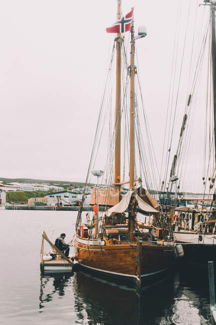 Blick auf großes Holzschiff im Hafen mit Matrose, der bei bewölktem Tag in der Nähe sitzt — Stockfoto
