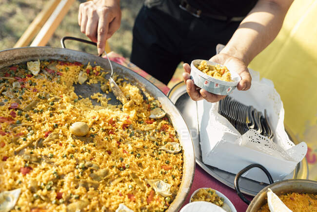 Cultivo cocinero irreconocible de pie en grandes sartenes y servir plato de paella. - foto de stock