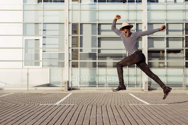 Young Africa-American man in hat jumping high while walking on street — Stock Photo