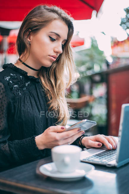 Retrato de una joven rubia hermosa en el teléfono móvil trabajando en el ordenador y tomando café - foto de stock