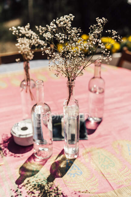 Piccoli fiori bianchi rustici in bottiglie di vino sul tavolo. — Foto stock