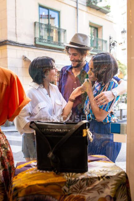 Junge Männer und Frauen lächeln und betrachten Kleidung in einem kleinen Geschäft, während sie auf der Straße in der Nähe von Schaufenstern stehen — Stockfoto