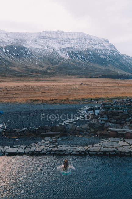 Vue de la femme nageant dans l'eau bleue du réservoir naturel avec des montagnes sur le fond — Photo de stock