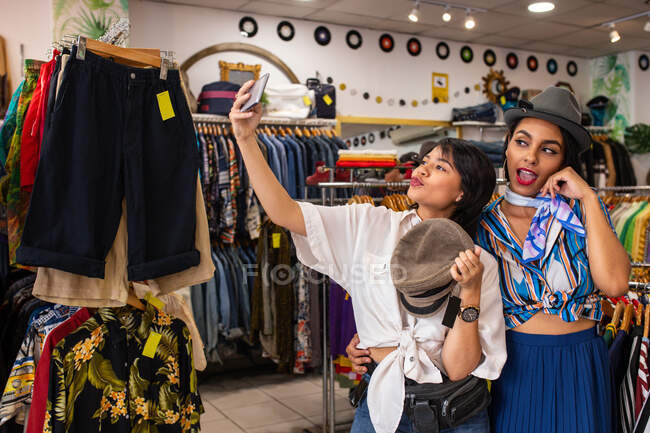 Amici allegri cercando sul cappello in negozio e prendendo selfie — Foto stock