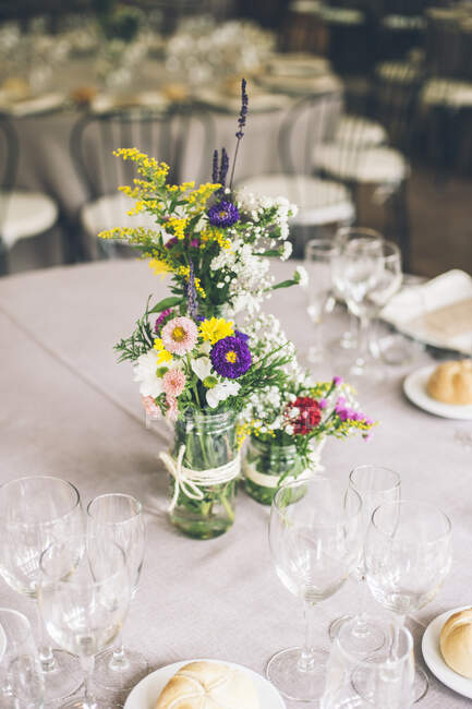 Hermosas flores rústicas brillantes en botella en la mesa de banquete servida. - foto de stock