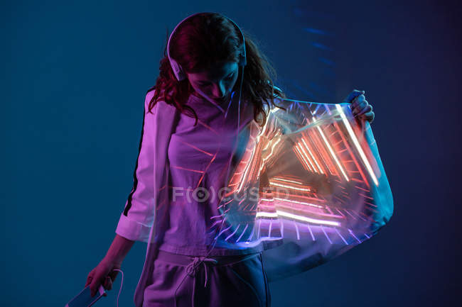 Jeune femme dans les écouteurs regardant la projection de lumière au néon sur blazer — Photo de stock