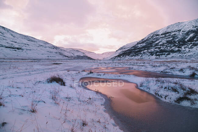 View of calm terrain with frozen lake under snow among mountains on background of sunset pink sky — Stock Photo