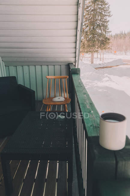 Vue extérieure du porche de la maison en bois avec tasse de café sur clôture et paysage enneigé sur fond — Photo de stock