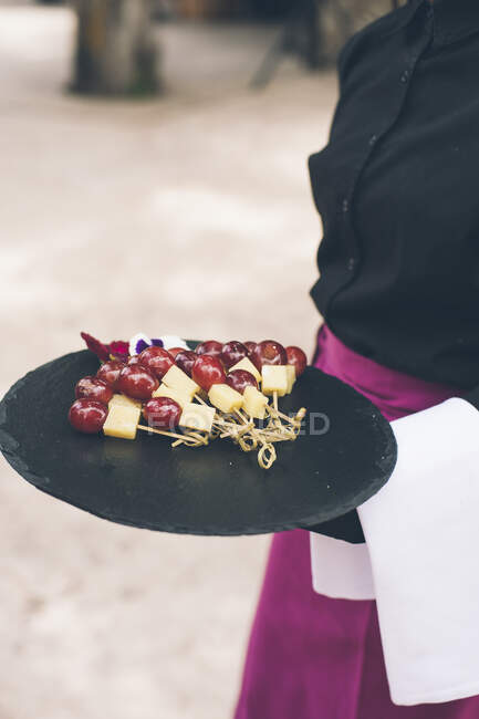 Serveur méconnaissable tenant plateau avec canape de raisin et fromage. — Photo de stock