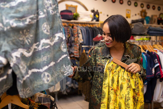 Jovem atraente à procura de roupa nova em trilhos de roupas em pequena loja — Fotografia de Stock