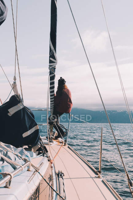 Вид ззаду жінка сидить на дзьобі вітрильного човна на холодній морській воді з горами на фоні — стокове фото