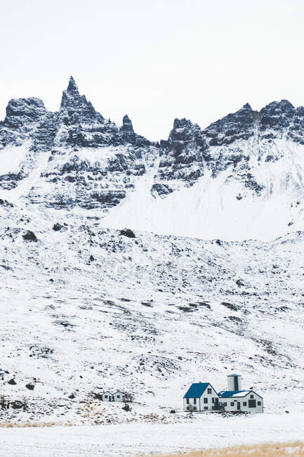 Vue sur les montagnes enneigées rocheuses avec des sommets et maison isolée ci-dessous en plein jour — Photo de stock