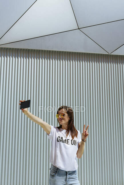 Весела жінка бере селфі і позує біля сучасної стіни — стокове фото