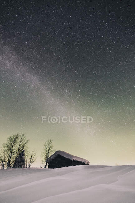 Vista de la cabaña de madera remota en la nieve pesada bajo el hermoso cielo estrellado - foto de stock