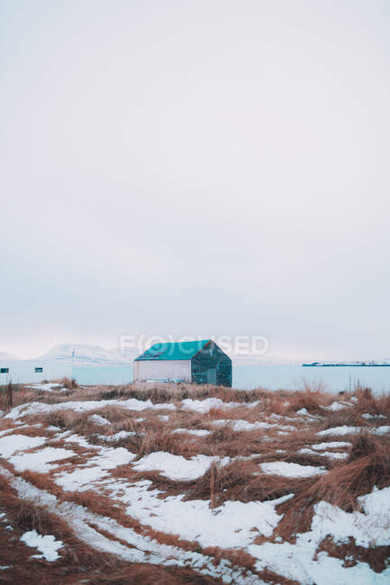 Vista de la pequeña cabaña en terreno seco y frío con nieve bajo el cielo sombrío - foto de stock