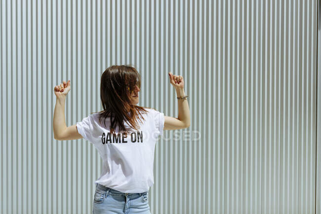 Lovely young lady snapping fingers and looking away while standing near metal wall and dancing on sunny day — Stock Photo