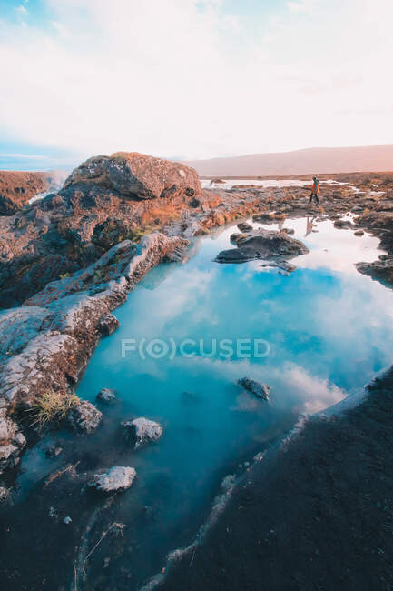 Pintoresca vista del agua azul entre las rocas que reflejan el cielo con el viajero caminando sobre piedras a la luz del día - foto de stock