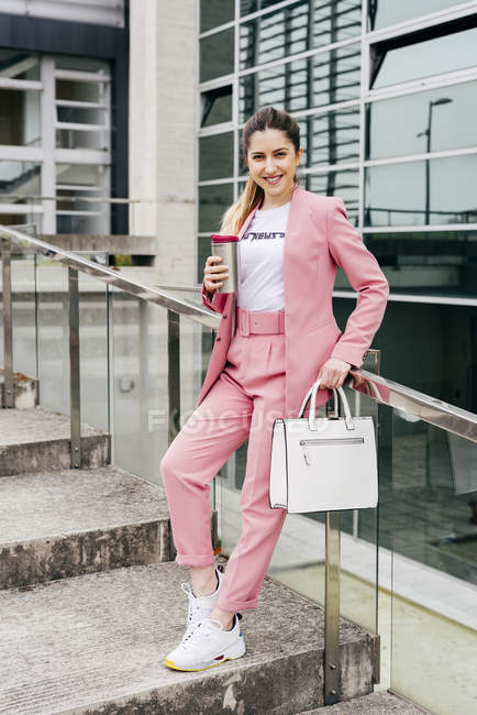 Mujer de moda con café de pie en los escalones y apoyado en la barandilla de metal - foto de stock