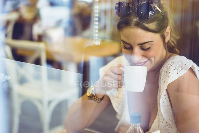 Молода красива жінка сидить у кафе посміхається і п'є каву? дивиться вниз — стокове фото