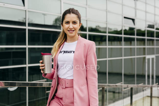 Модная молодая женщина с кофе стоит перед современным офисным зданием — стоковое фото