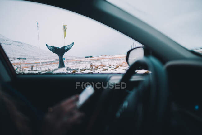 Shot from inside of car traveling on remote snowy terrain with whale tail sculpture on roadside — Stock Photo
