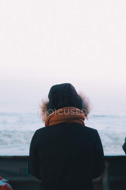 Rückansicht einer Frau in warmer Kleidung mit Kapuze, die an Deck eines Schiffes steht, das in kalter See segelt — Stockfoto