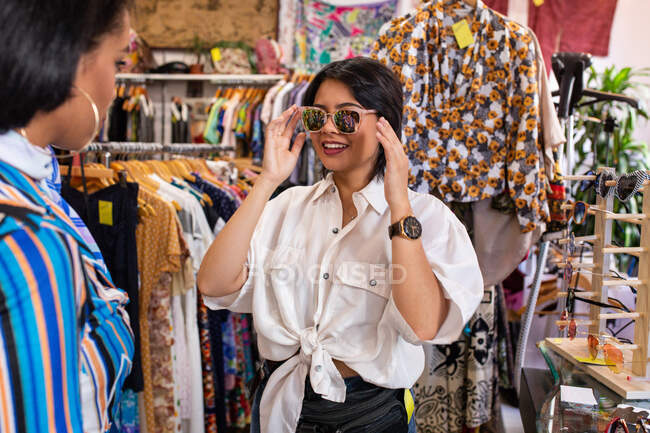 Bella giovane femmina sorridente e raccogliendo occhiali da sole da piccolo negozio — Foto stock