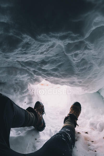 Schnappschuss der Beine eines Reisenden in Stiefeln, der in einer verschneiten Höhle mit Licht unten sitzt — Stockfoto