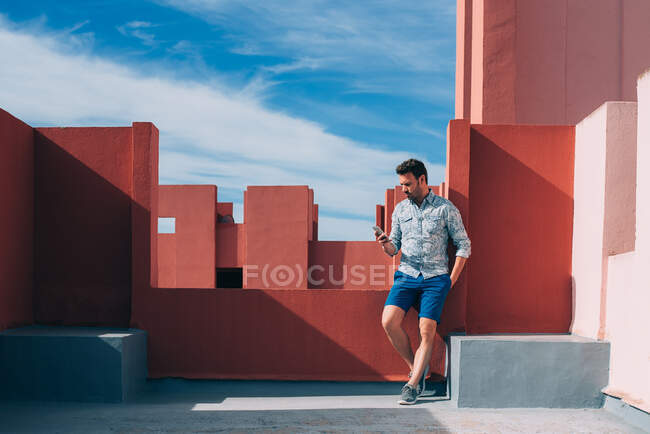Man leaning in a colorful rooftop building with mobile phone — Stock Photo