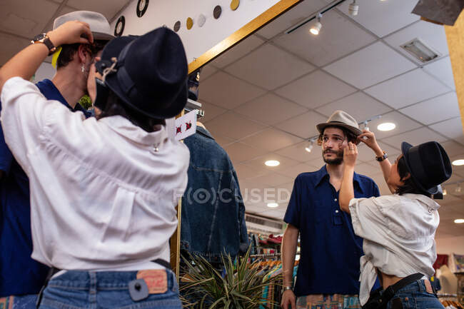 Amigos alegres probándose el sombrero en la tienda - foto de stock