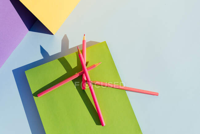Розовые карандаши на зеленой книге, в пространстве геометрических форм и сильных теней. Снова в школу — стоковое фото