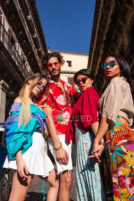 Нахабний молодий чоловік, який обіймає трьох жінок, одягає модний одяг і стоїть на вулиці в сонячний день. — стокове фото