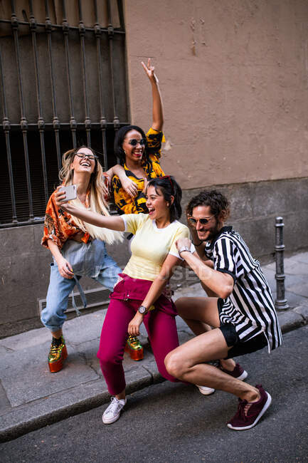 Groupe de jeunes en tenue tendance riant et prenant du selfie tout en s'amusant dans la rue de la ville — Photo de stock