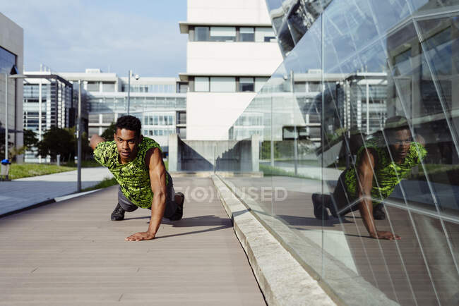 Adult ethnic man doing push-ups exercise with one arm while working out on city street — Stock Photo