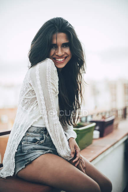 Портрет улыбающейся молодой женщины, сидящей на балконе — стоковое фото