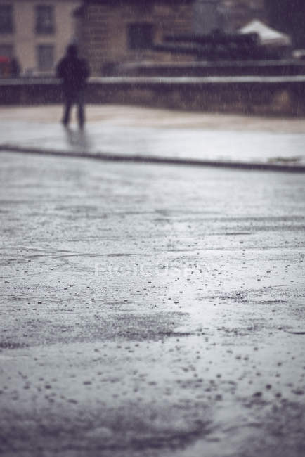Primo piano di gocce di pioggia su strada di Parigi durante pioggia su sfondo di persona che cammina in vestiti neri — Foto stock